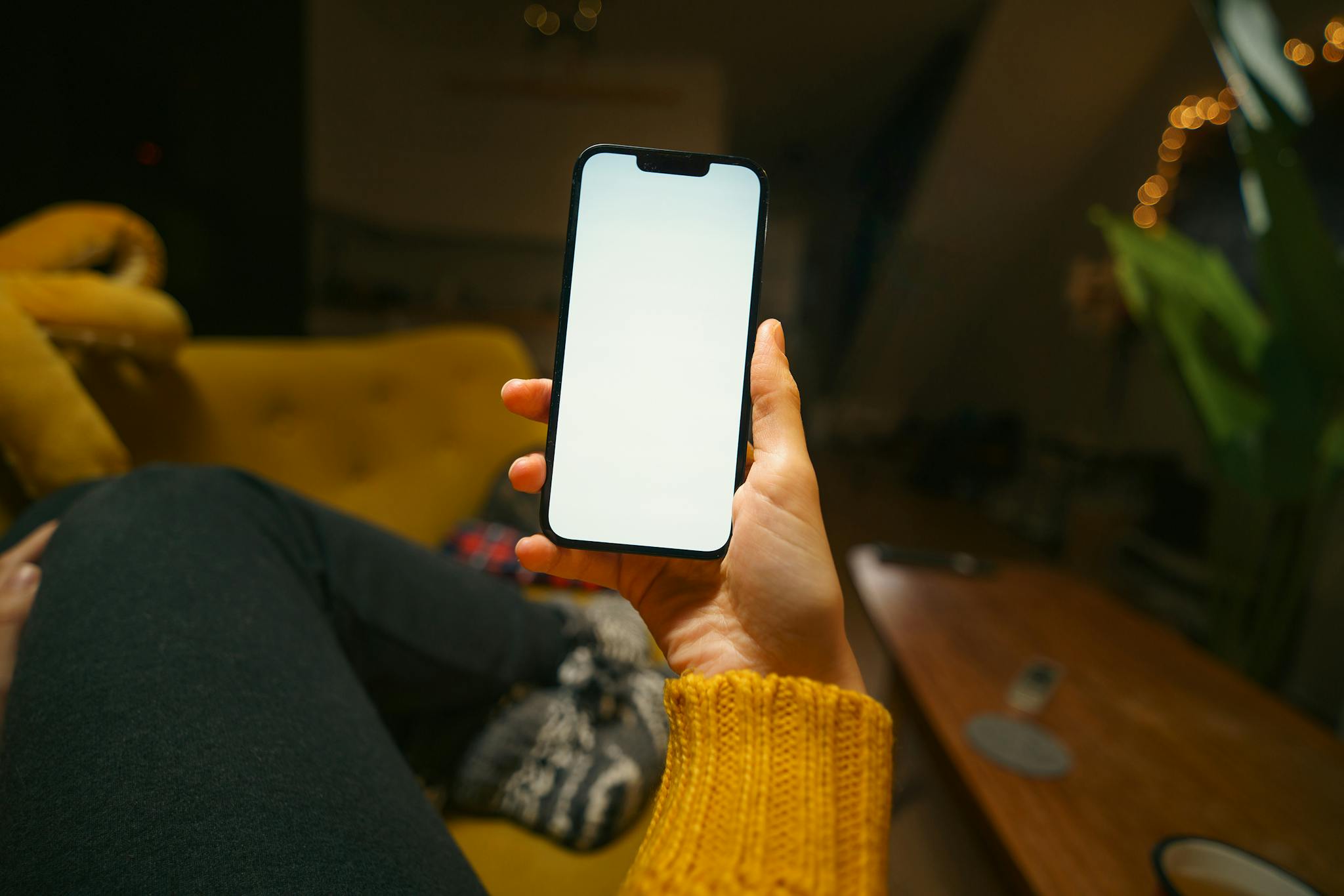 Relaxing at home with a smartphone showing a blank screen on a cozy sofa in a stylish living room.