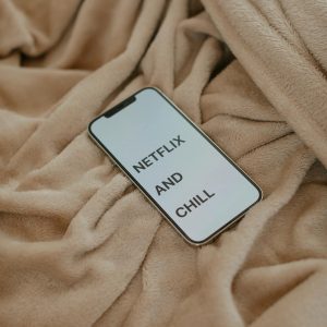 Smartphone displaying 'Netflix and Chill' on a beige blanket, ideal for cozy lifestyle themes.