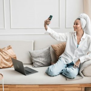 Smiling woman with a head towel takes a selfie in a comfy living room setting.