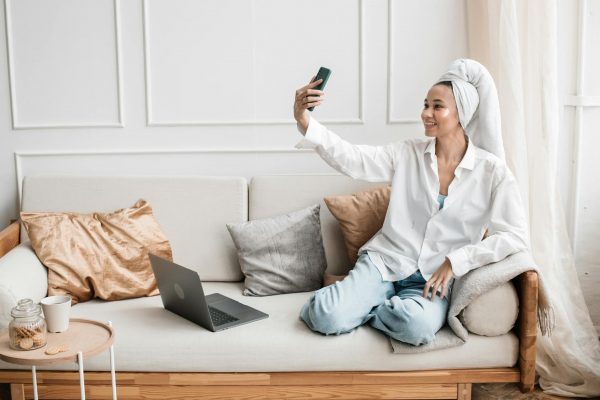 Smiling woman with a head towel takes a selfie in a comfy living room setting.