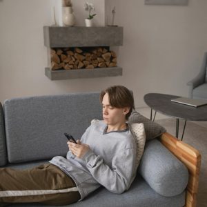 Young man using smartphone while relaxing on a modern gray sofa in a stylish living room.