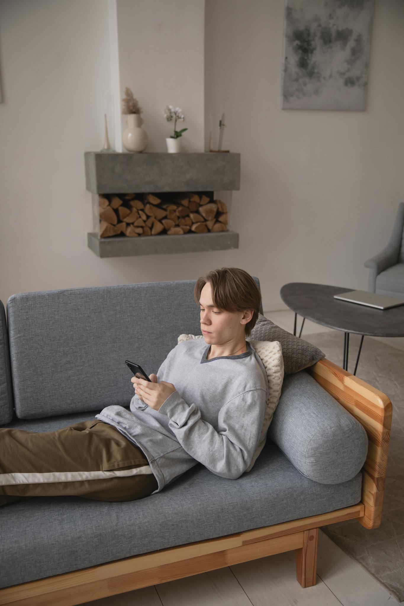 Young man using smartphone while relaxing on a modern gray sofa in a stylish living room.